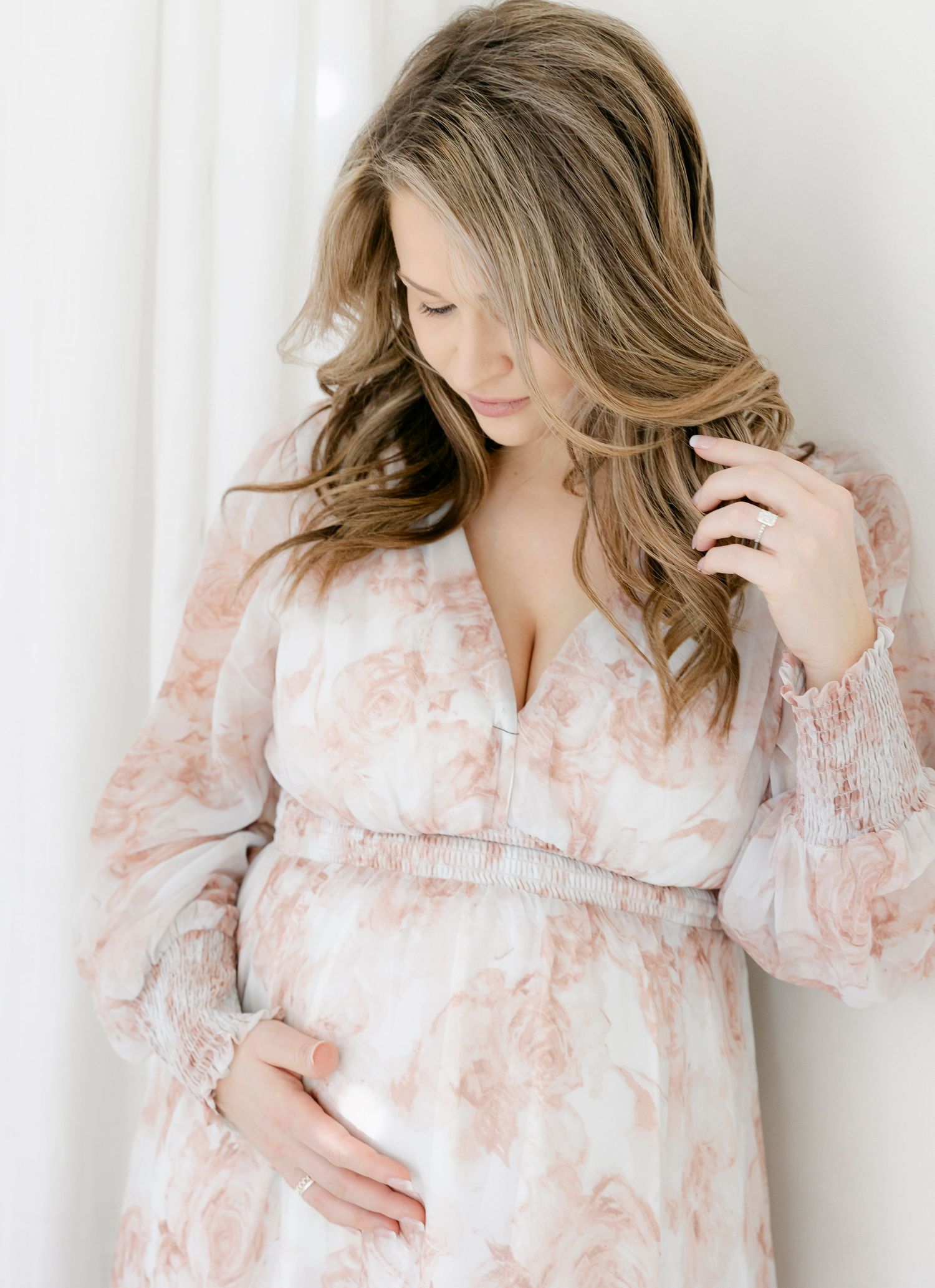 Black and white photo of a pregnant woman standing by large arched windows, cradling her baby bump in natural light.
