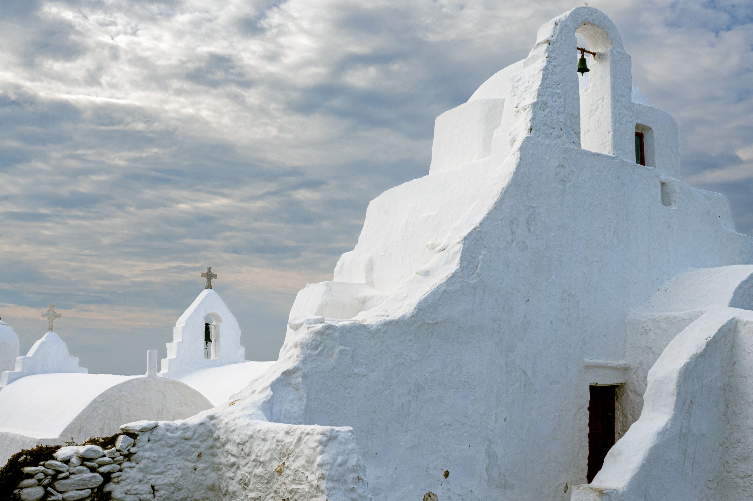 A row of whitewashed Greek Orthodox churches with traditional blue domes against a cloudy Mediterranean sky.