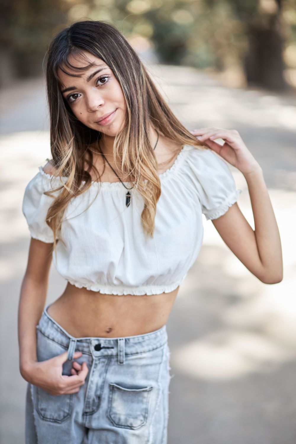 Model in cropped white peasant top and denim poses outdoors with soft natural lighting.