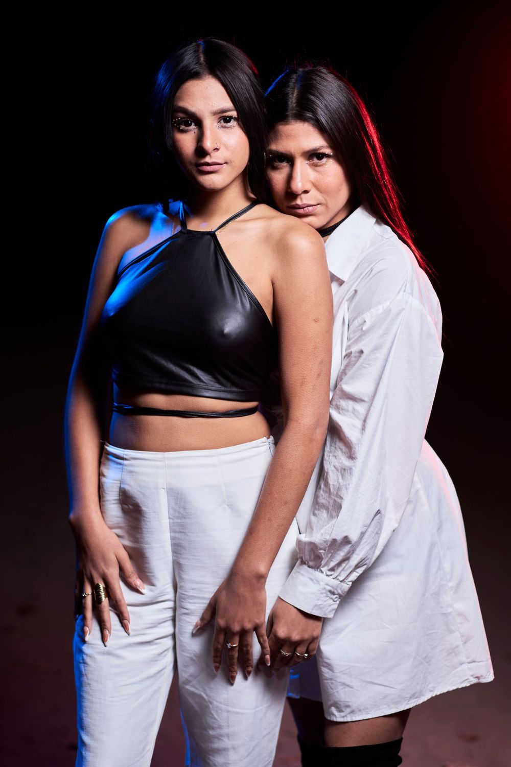 Two models pose together in contrasting black and white outfits with dramatic studio lighting.