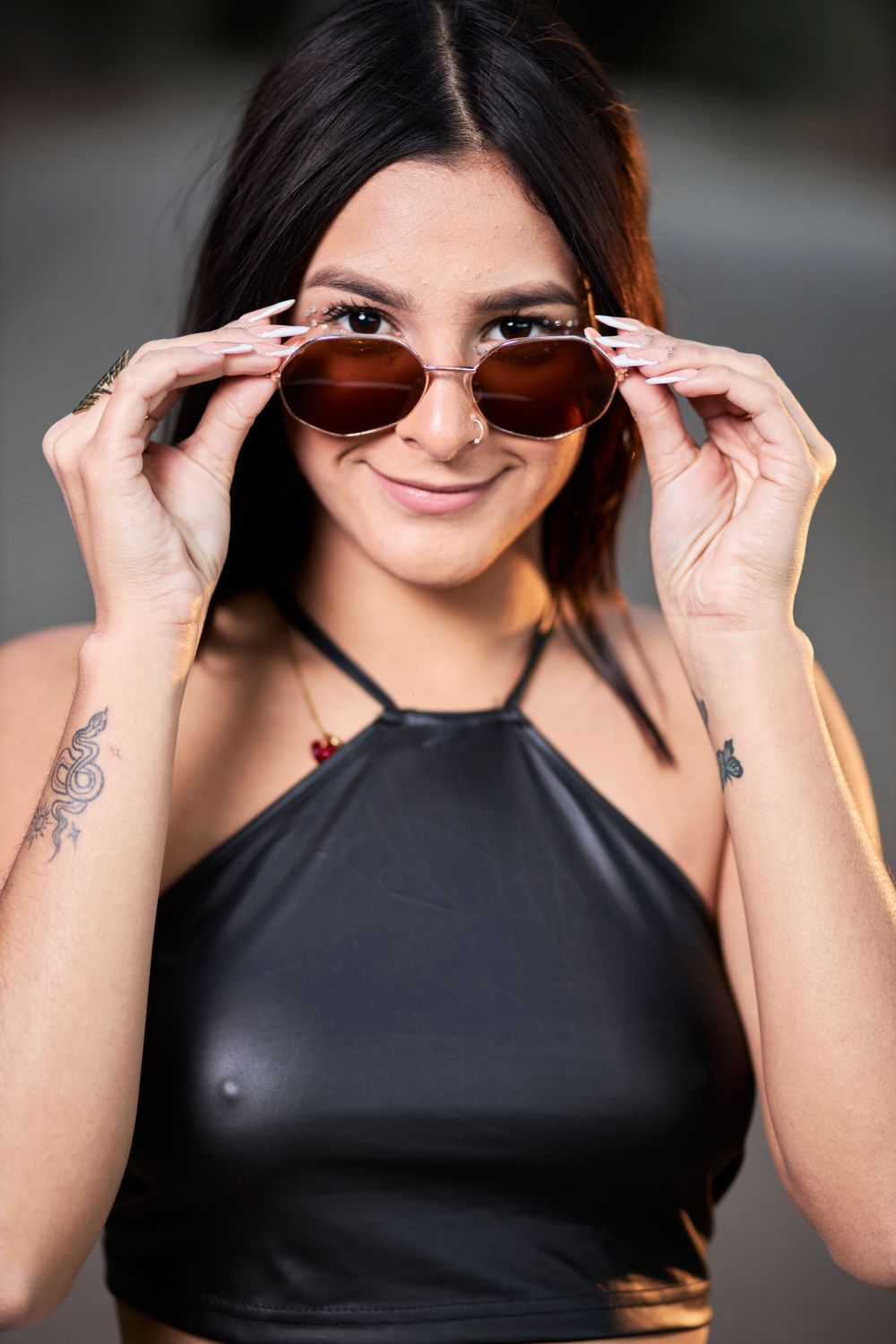 Model in black halter top adjusting sunglasses while posing outdoors.