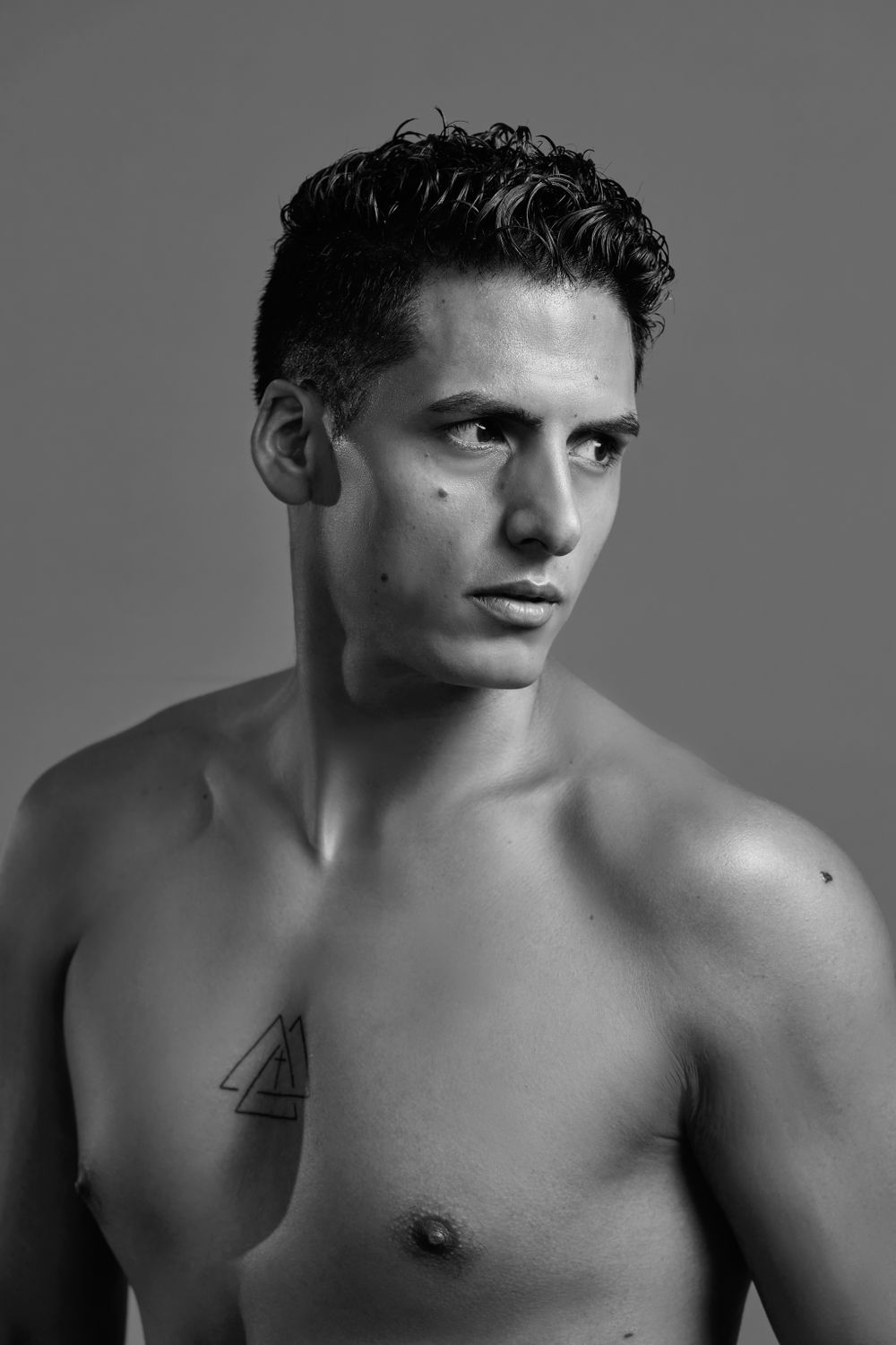 Black and white portrait showing muscular physique with geometric tattoo.