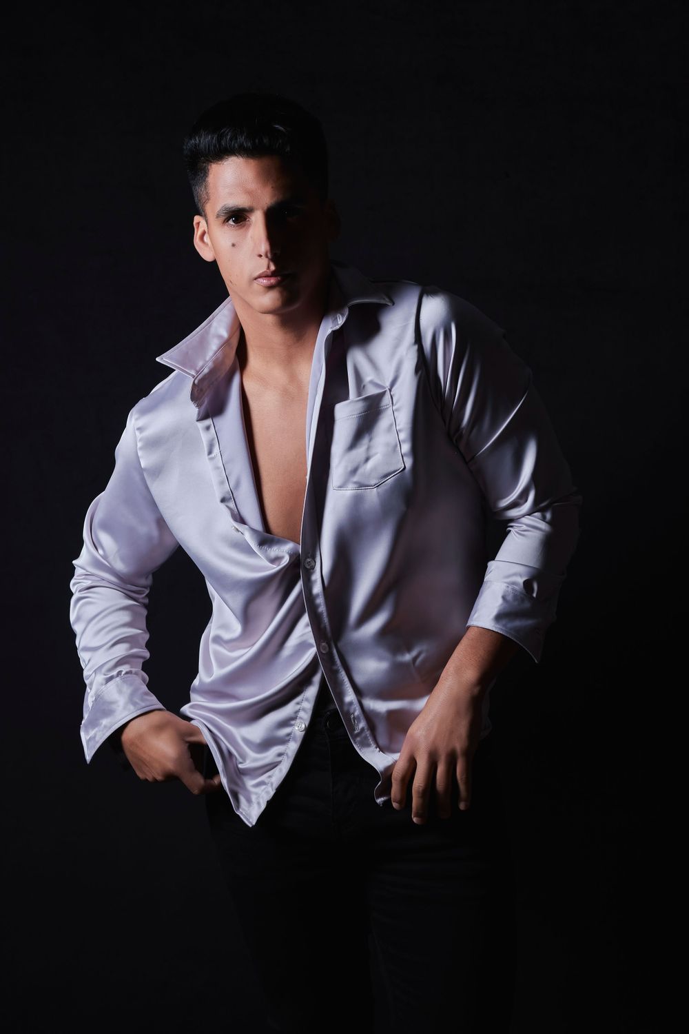 Dramatic portrait in open white shirt against dark background with moody lighting.