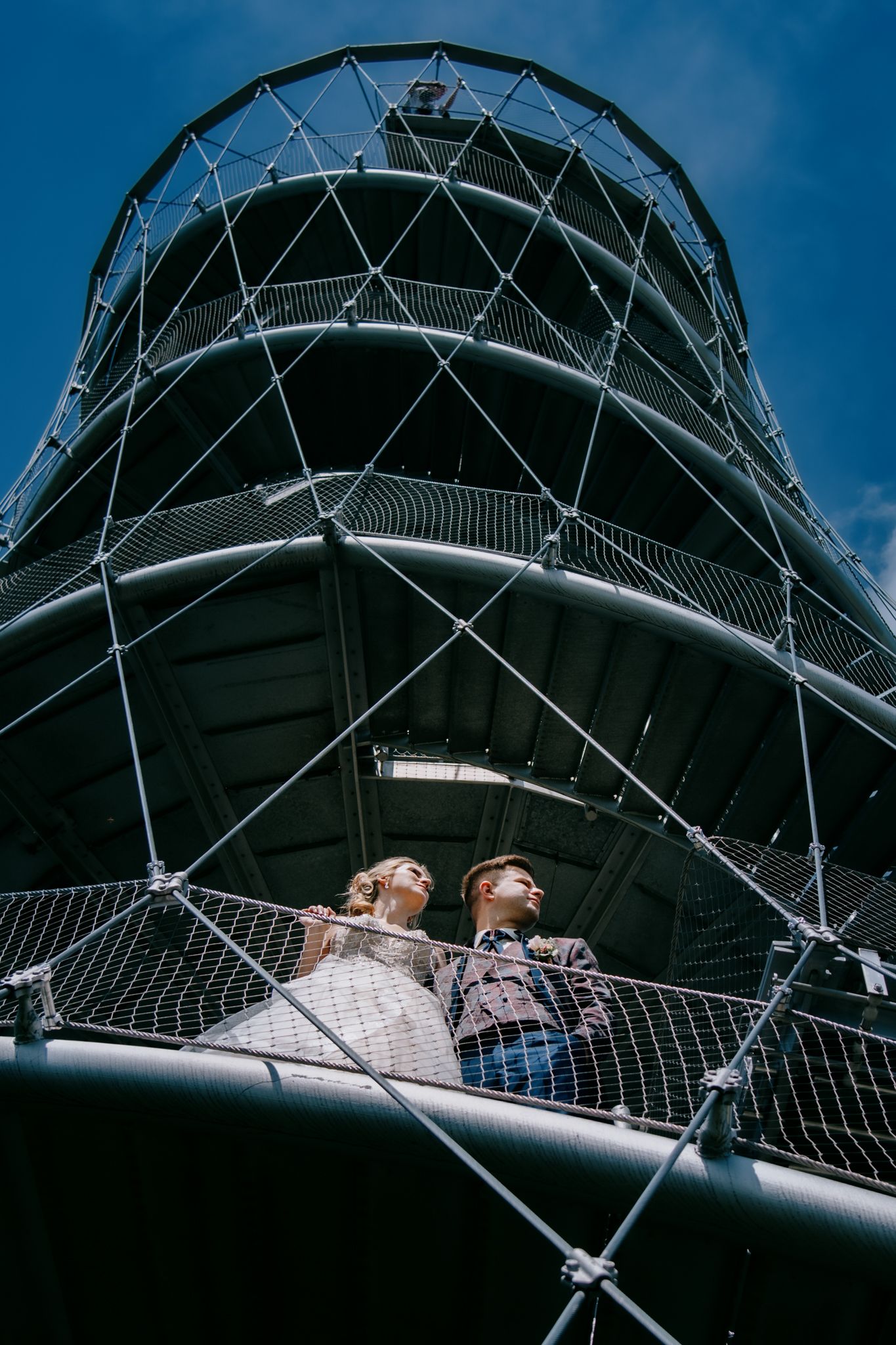 A dramatic upward view of a modern tower structure with geometric metal framework against blue sky.