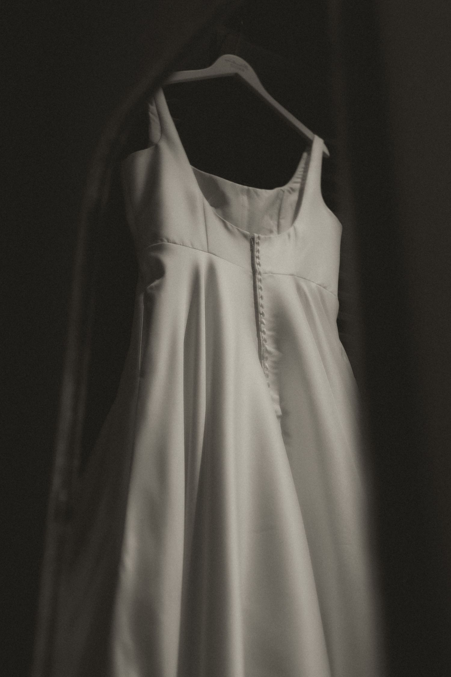 A close-up view of a white wedding dress hanging on a dark background.