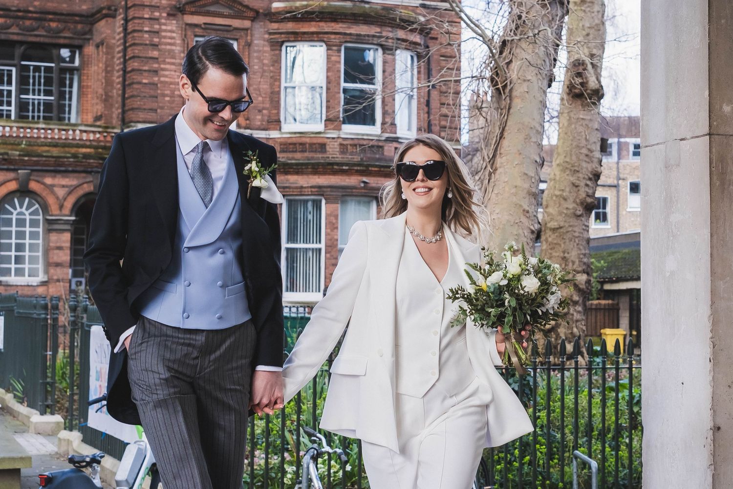 A well-dressed couple walking together in front of a historic brick building.