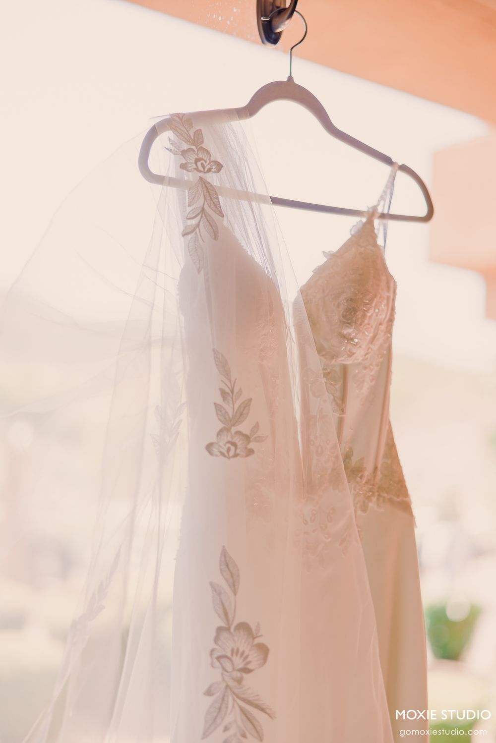 White wedding dresses hanging on hangers in a sunlit room with a warm peachy glow.