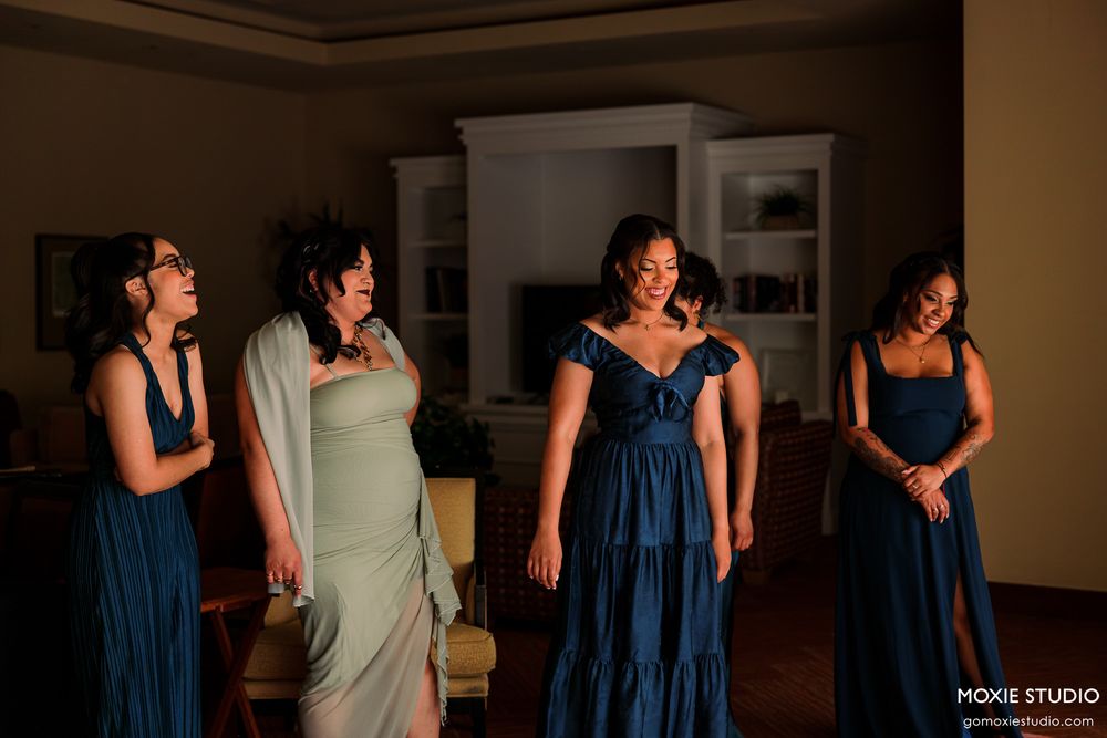 A group of people in blue dresses and formal attire dance together in a dimly lit indoor space.