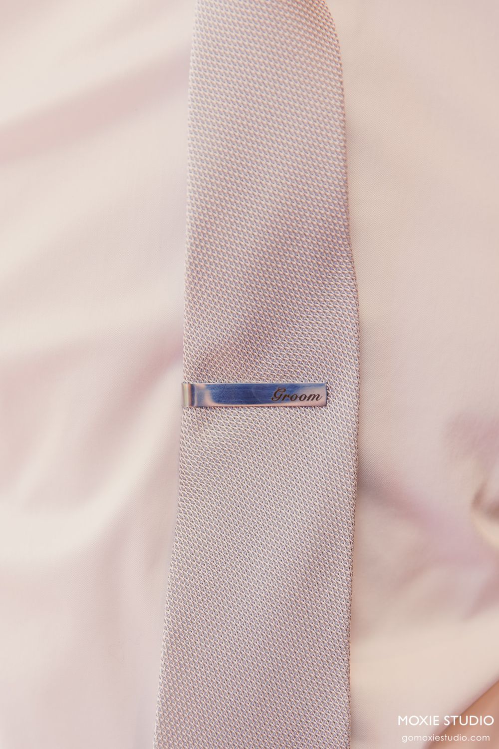Close-up detail shot of a white textured tie with a small blue tie clip accent.