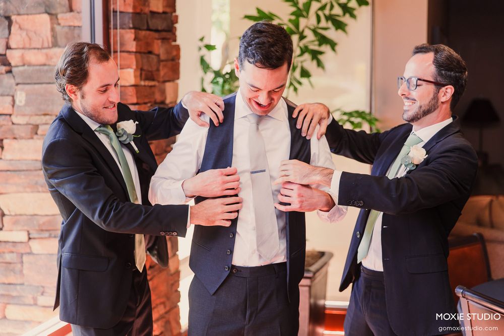 A group in formal wear laughs and embraces during a celebratory moment indoors.