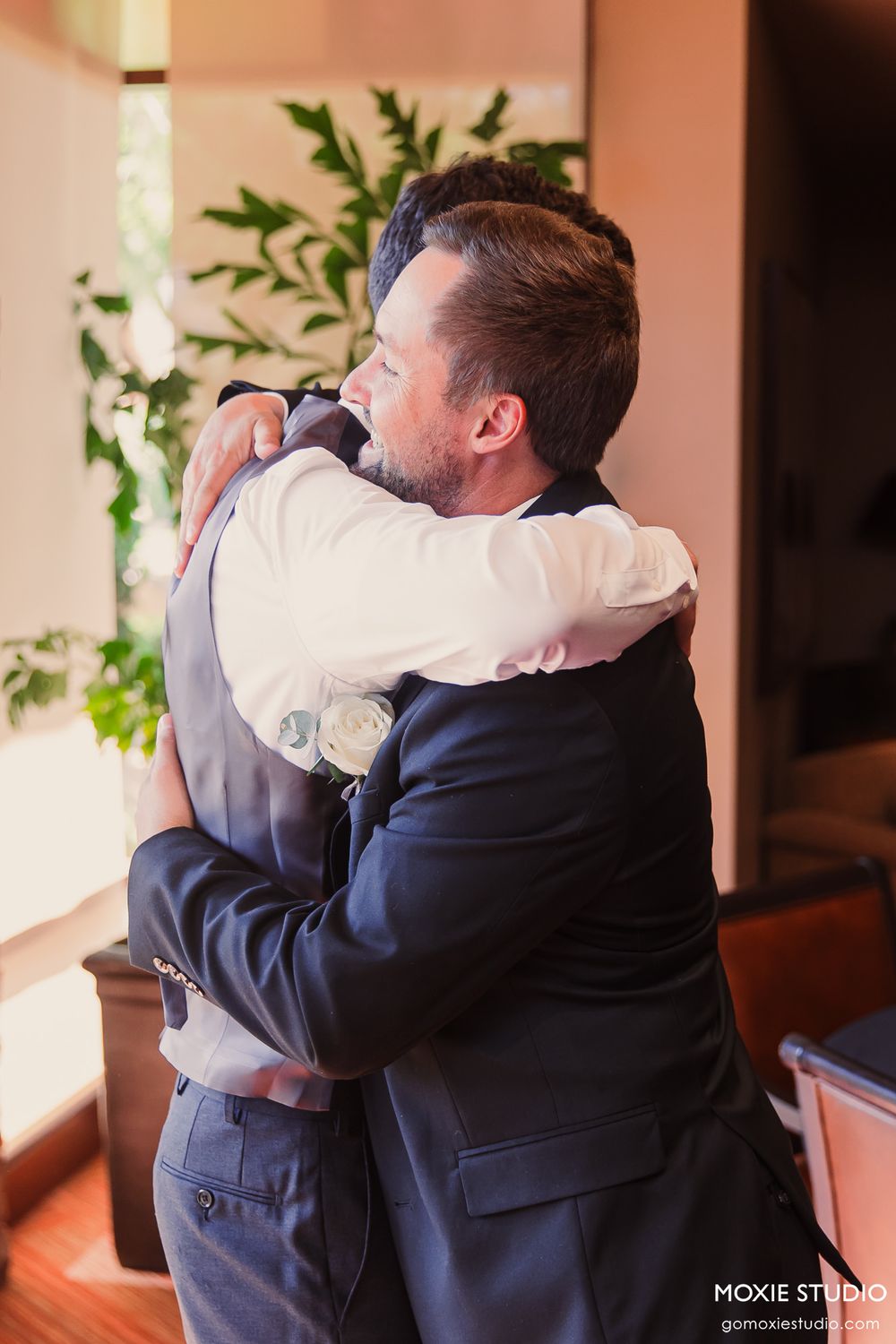 Two people in formal attire share an emotional embrace during what appears to be a wedding moment.