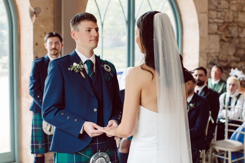 A bride and groom share their first dance at a rustic stone venue with large windows and guests watching.