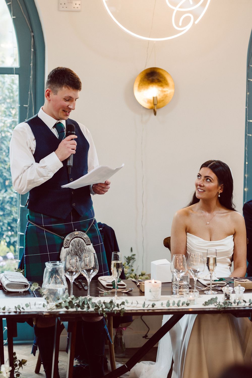 Wedding reception scene at head table with guests and speakers during emotional speeches at an elegant venue.