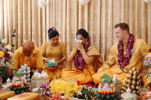 Buddhist monks in saffron robes sit at a long table performing a traditional ceremony with offerings and decorations.