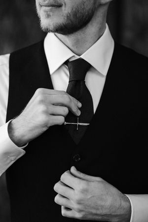 Black and white photo of hands adjusting a dark tie against a formal suit vest and white dress shirt.