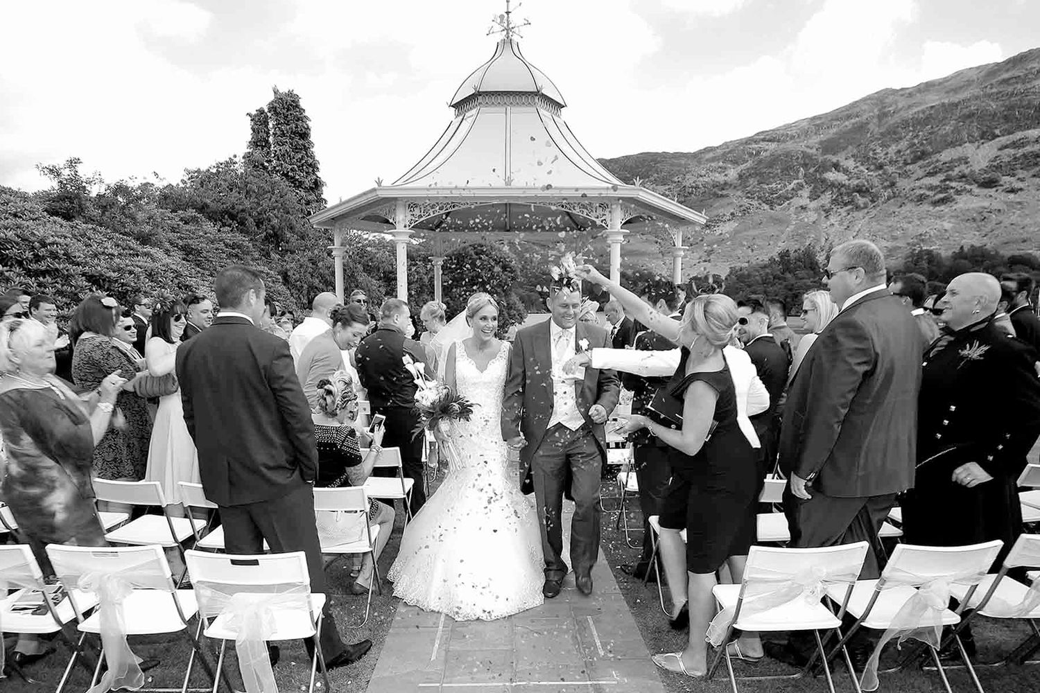A black-and-white photograph of an outdoor wedding ceremony at the lakeside gazebo at Inn on the Lake, Ullswater.