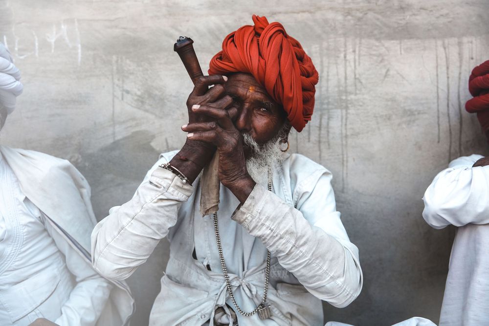 Elderly Indian man in red turban smoking a traditional pipe in a candid street photography portrait.
