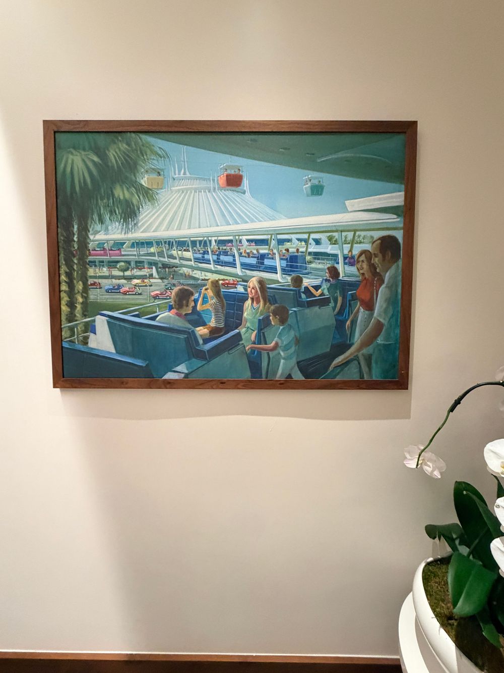 A series of panoramic paintings depicting poolside and beach scenes hang on a white wall above tropical plants.