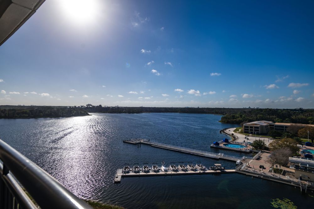 Panoramic aerial view of a marina and coastline with boats under bright sunlight reflecting off calm ocean waters.