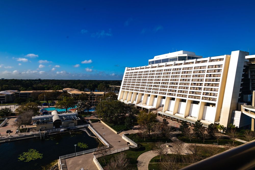 Aerial view of a modern hotel resort complex with multiple buildings and swimming pools under bright blue sky.