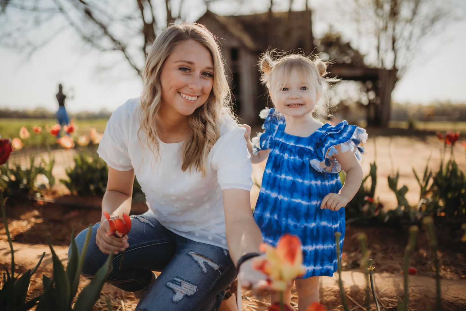 A family enjoys a casual outdoor photo session in a rustic garden setting with natural lighting and blue tie-dye clothing.