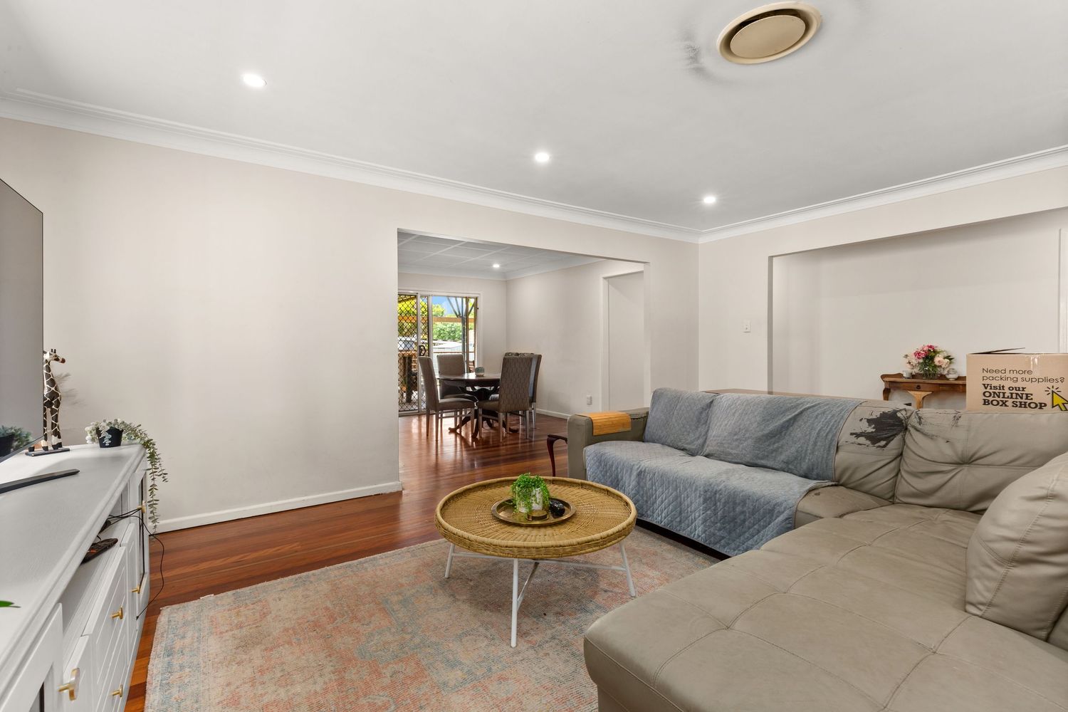 Spacious living room with grey sectional sofa, timber floors, and open plan dining area visible in background.