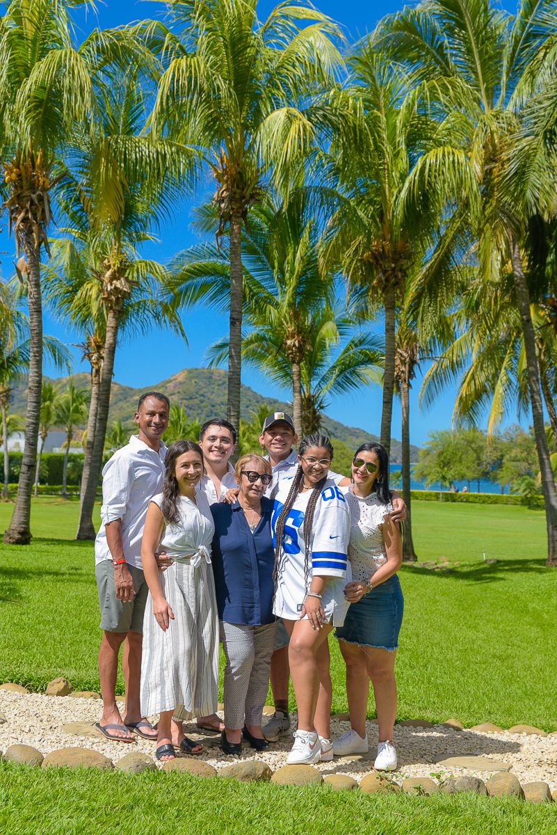 A group poses together on a sunny day with palm trees and mountains in the background at a tropical resort.