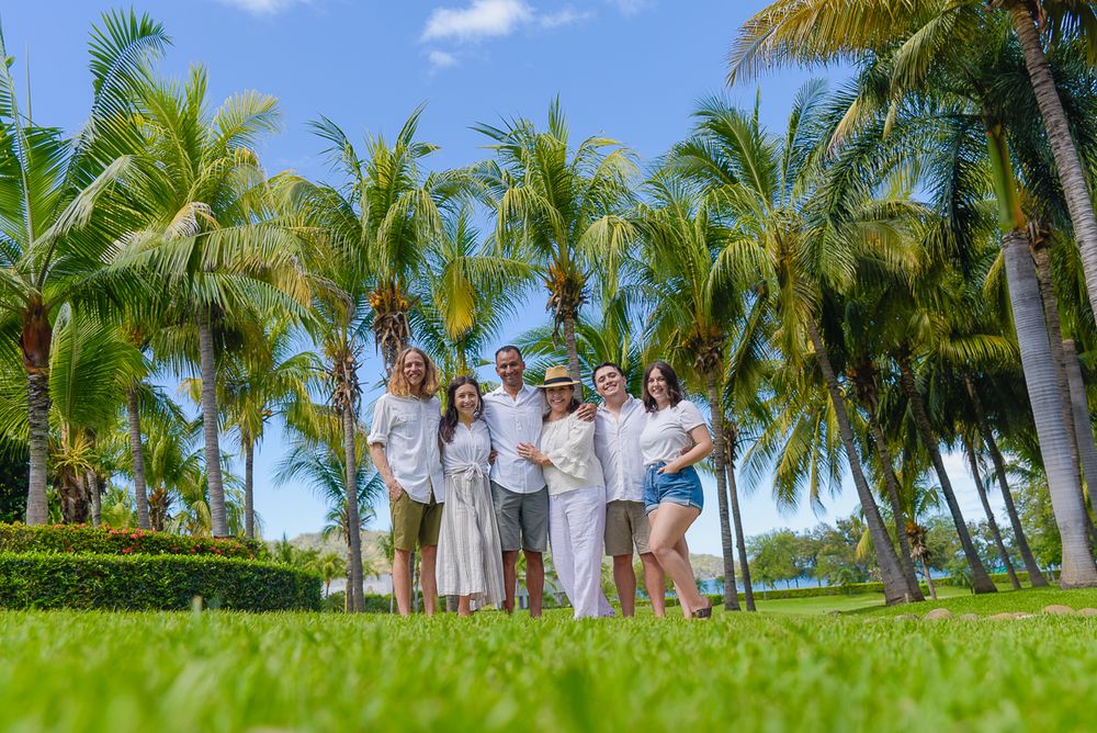Group of people posing together on a lush green lawn surrounded by tall palm trees on a sunny day.