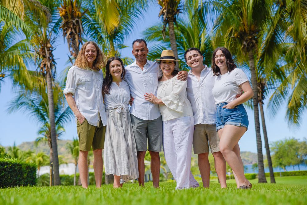Family gathering on a lush green lawn surrounded by tall palm trees under bright blue skies.