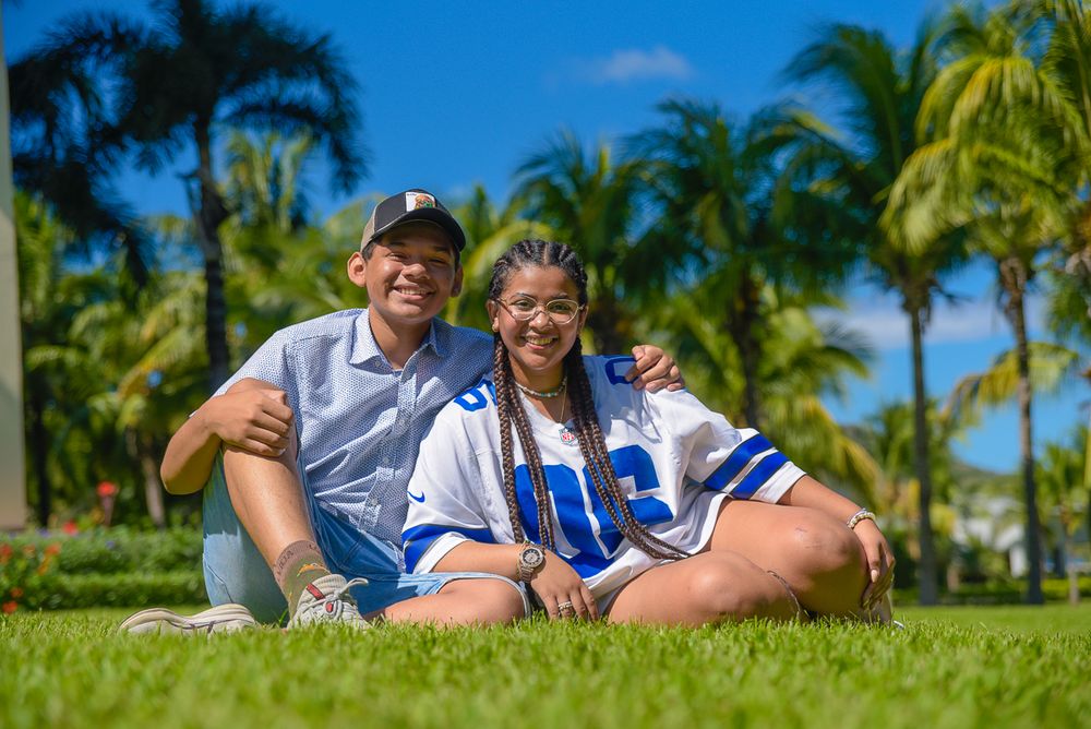 Two people relax on green grass with palm trees in a tropical setting.