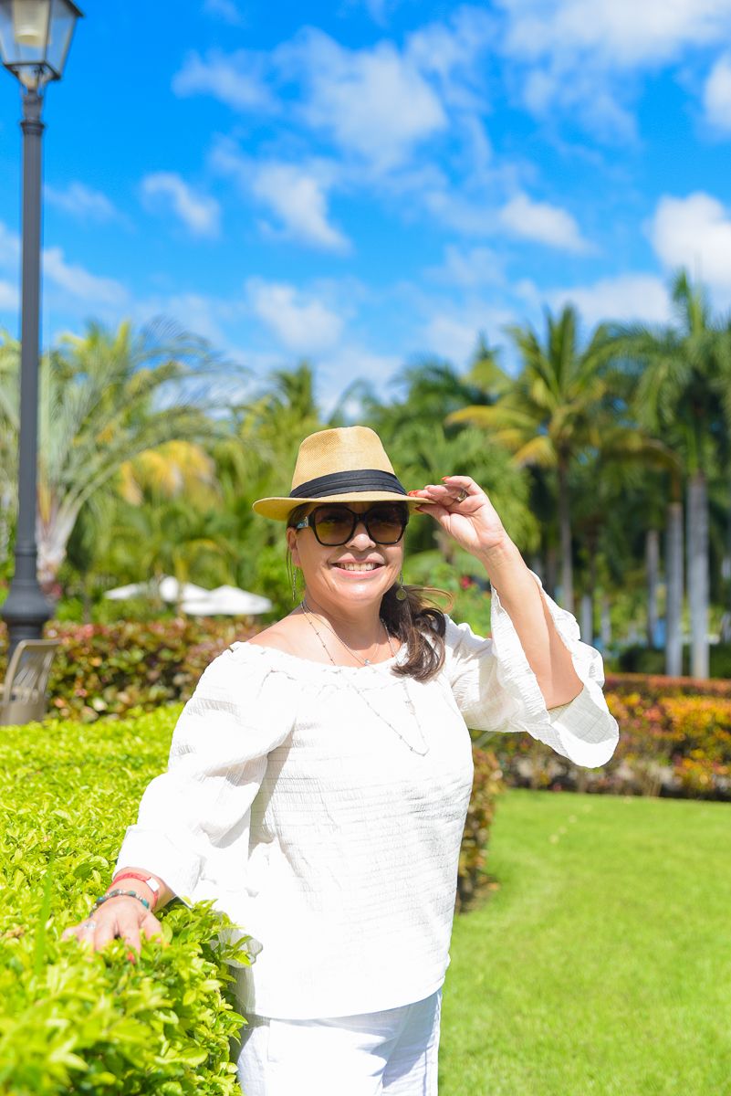 Person in white outfit and sunhat enjoying a bright sunny day in a tropical garden with palm trees and lush greenery.