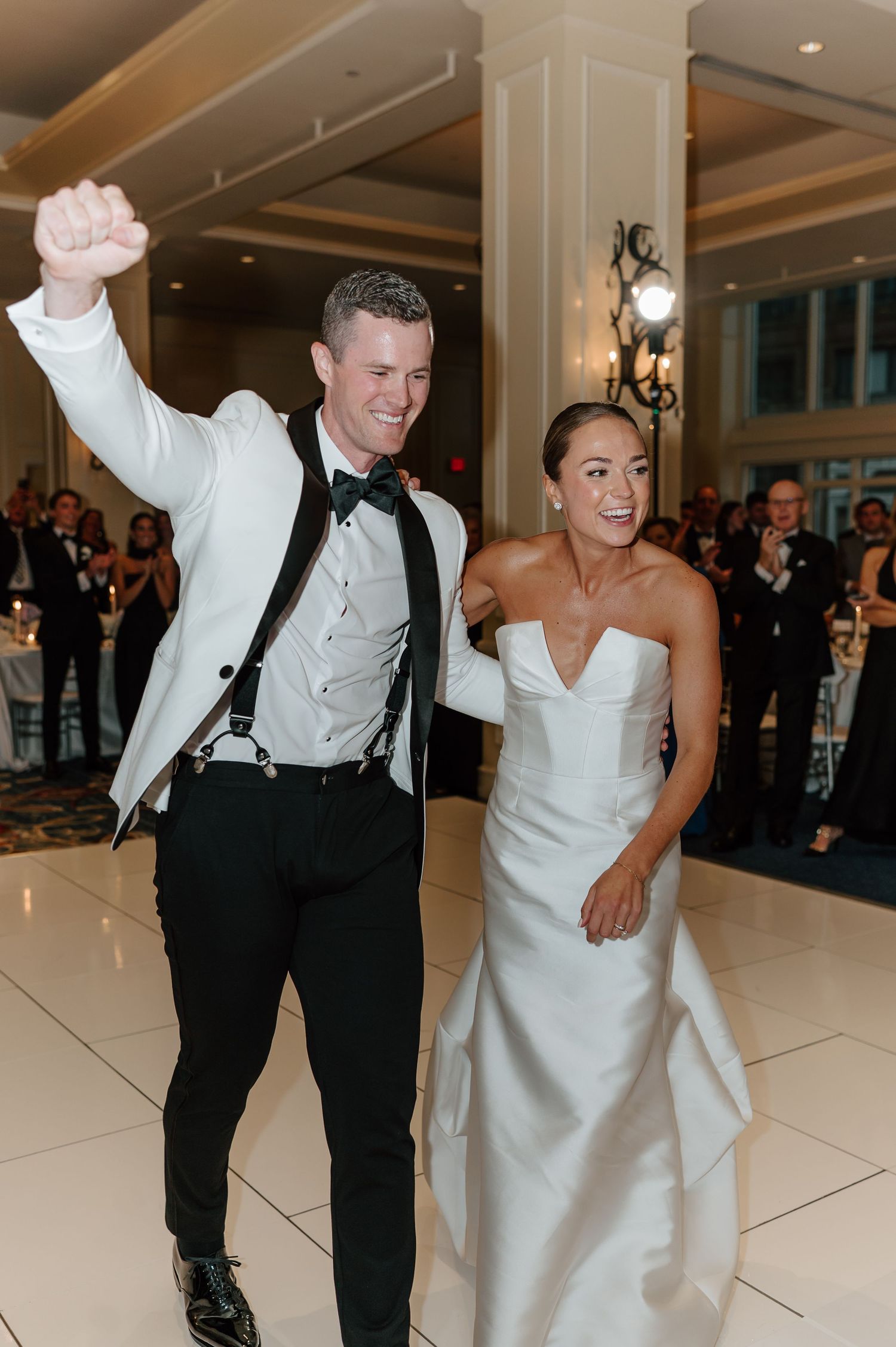Wedding reception guests dancing and celebrating on an elegant blue patterned carpet in a ballroom with chandeliers.