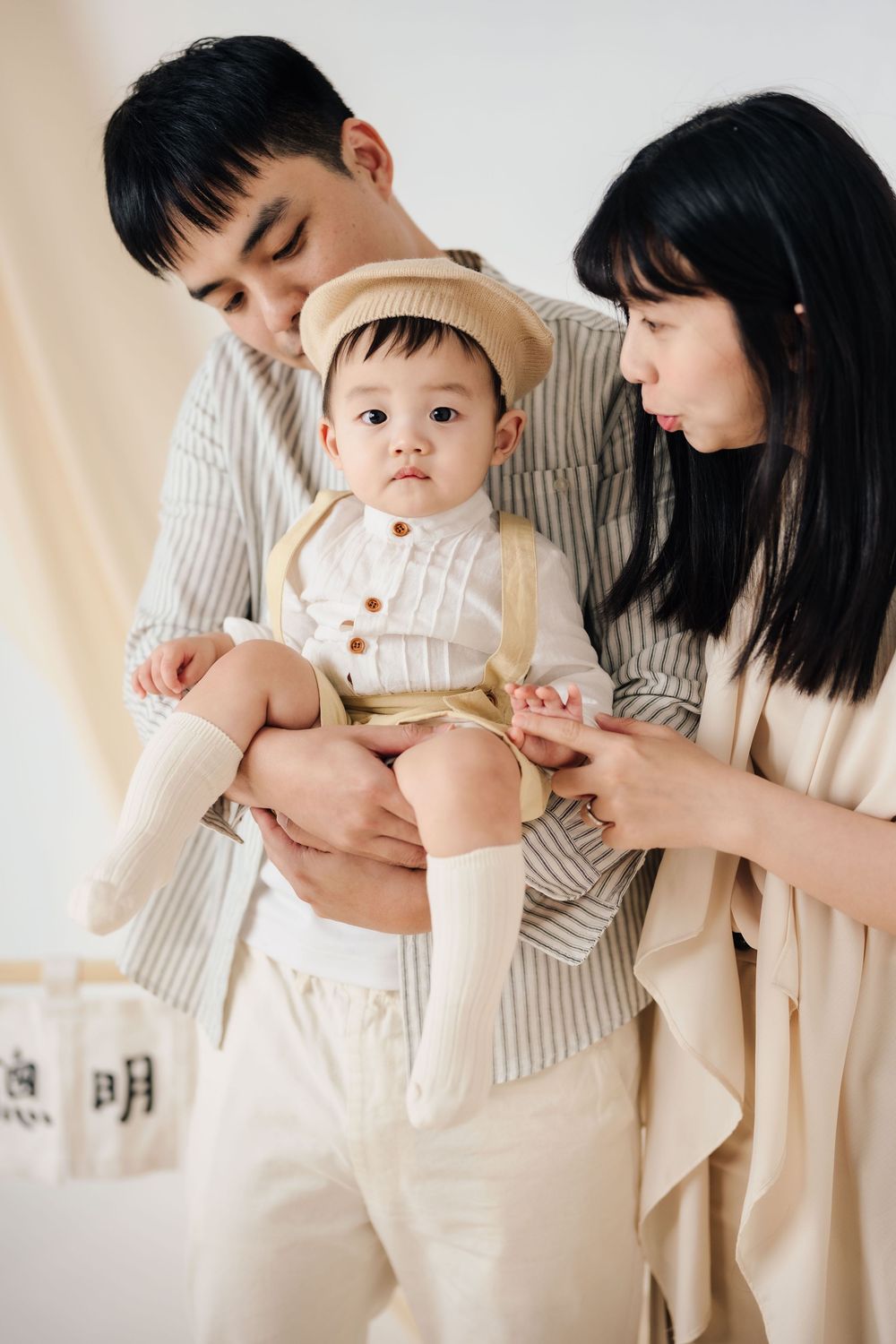 抓周寫真、全家福，渴望影像紀錄一歲寶寶抓周儀式與親子互動，透過自然光棚拍呈現溫暖氛圍，畫面包含寶寶拿取抓周物品、爬行探索與父母陪伴互動，整體風格乾淨柔和、色調溫潤，適合尋找屏東抓周寫真、全家福攝影、寶寶周歲紀念攝影的家庭參考，依照服裝而改變佈景，呈現真實自然且具故事感的家庭影像。