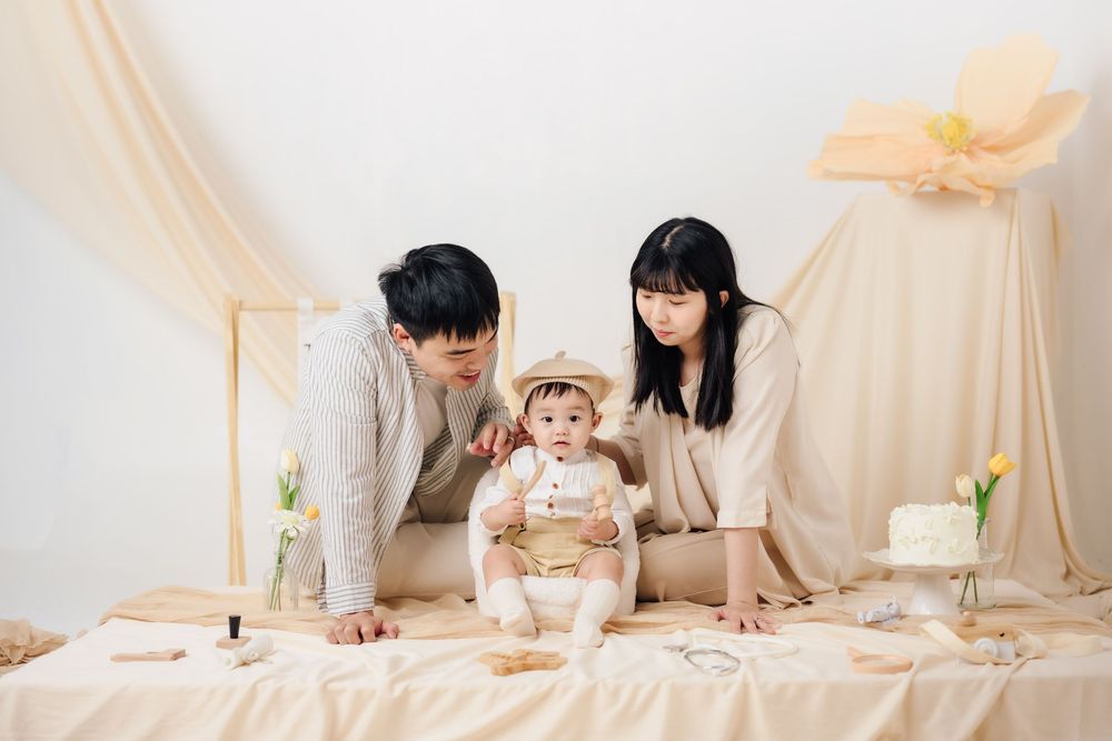 抓周寫真、全家福，渴望影像紀錄一歲寶寶抓周儀式與親子互動，透過自然光棚拍呈現溫暖氛圍，畫面包含寶寶拿取抓周物品、爬行探索與父母陪伴互動，整體風格乾淨柔和、色調溫潤，適合尋找屏東抓周寫真、全家福攝影、寶寶周歲紀念攝影的家庭參考，依照服裝而改變佈景，呈現真實自然且具故事感的家庭影像。