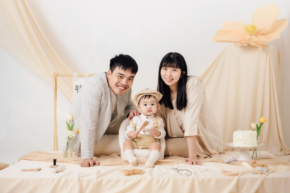 抓周寫真、全家福，渴望影像紀錄一歲寶寶抓周儀式與親子互動，透過自然光棚拍呈現溫暖氛圍，畫面包含寶寶拿取抓周物品、爬行探索與父母陪伴互動，整體風格乾淨柔和、色調溫潤，適合尋找屏東抓周寫真、全家福攝影、寶寶周歲紀念攝影的家庭參考，依照服裝而改變佈景，呈現真實自然且具故事感的家庭影像。