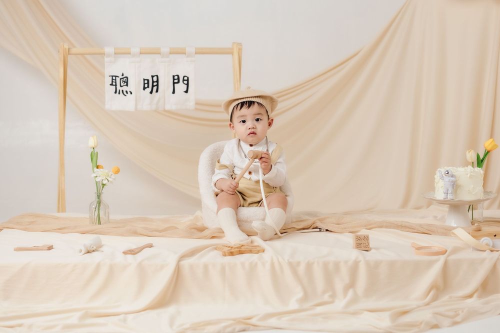 抓周寫真、全家福，渴望影像紀錄一歲寶寶抓周儀式與親子互動，透過自然光棚拍呈現溫暖氛圍，畫面包含寶寶拿取抓周物品、爬行探索與父母陪伴互動，整體風格乾淨柔和、色調溫潤，適合尋找屏東抓周寫真、全家福攝影、寶寶周歲紀念攝影的家庭參考，依照服裝而改變佈景，呈現真實自然且具故事感的家庭影像。