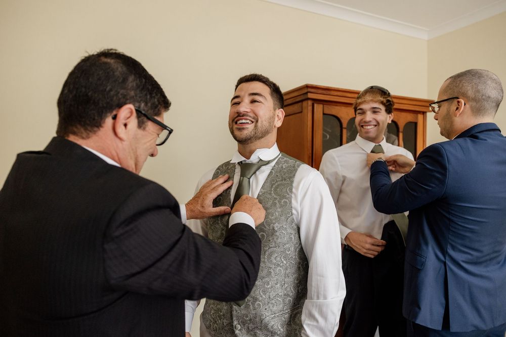 Four men in formal attire are conversing and interacting in an indoor setting.