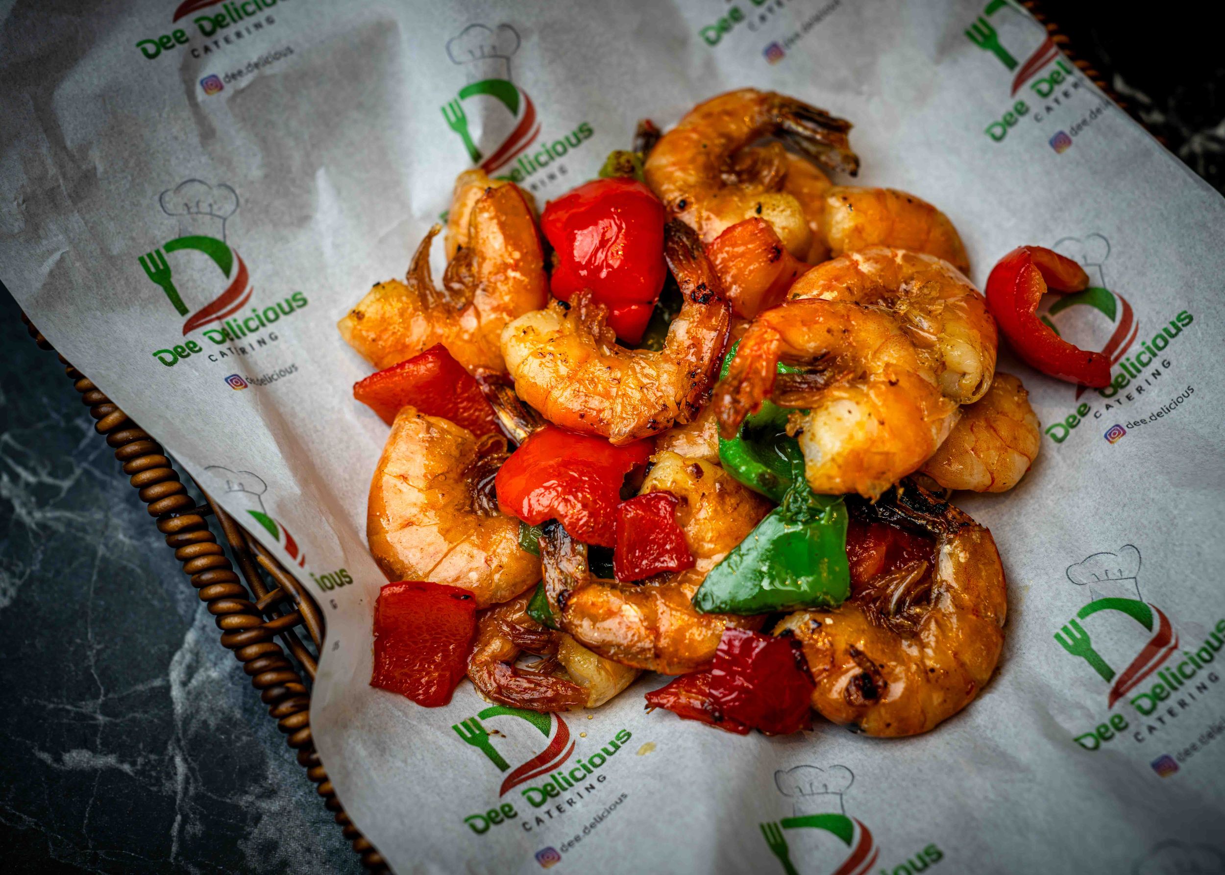 Spicy stir-fried shrimp with red and green bell peppers served on white deli paper in a basket.