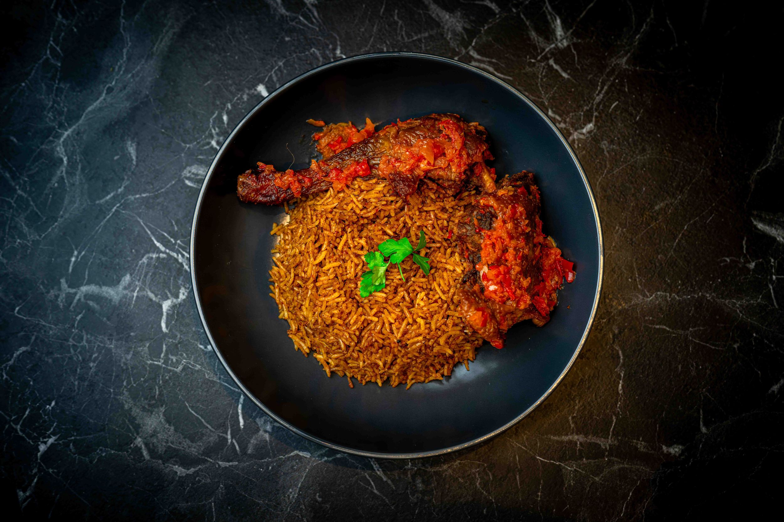 Spiced tomato rice served with crispy fried chicken in rich red sauce, garnished with fresh herbs on a black plate.