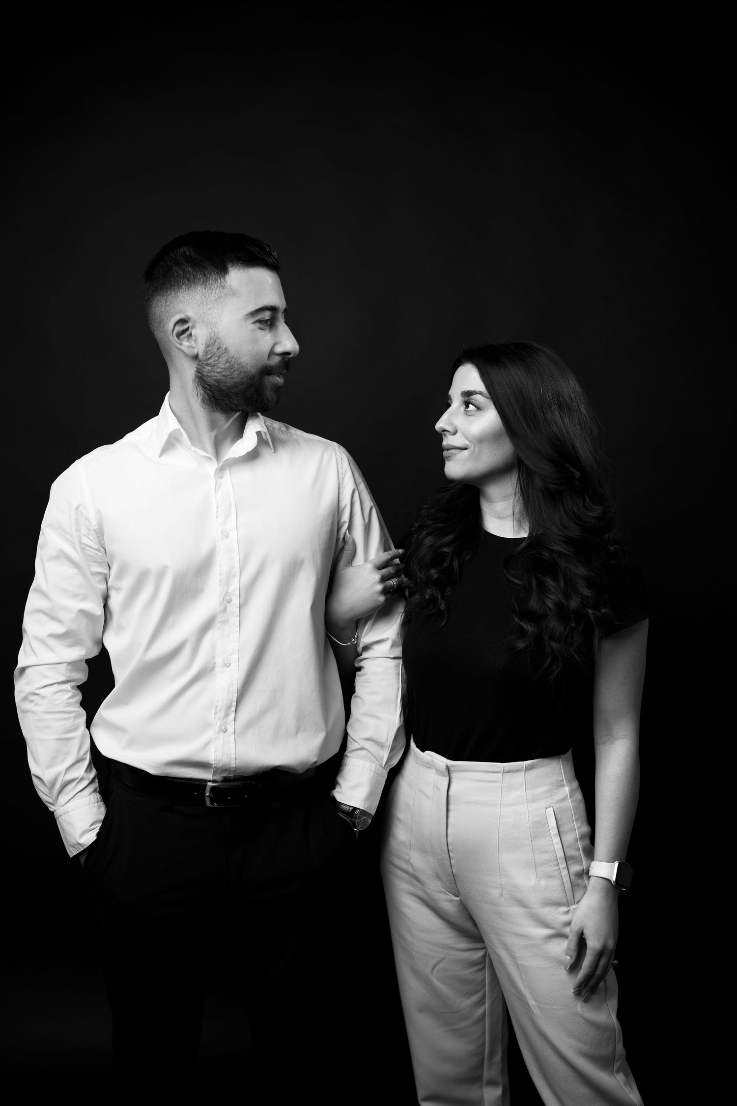 Black and white portrait of a couple in contrasting outfits against dark background.