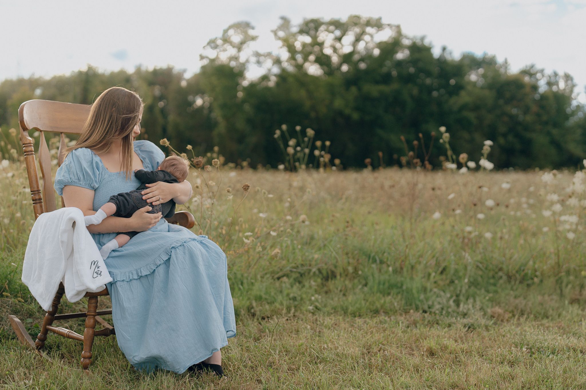 A romantic countryside photo shoot in Cuyahoga Falls, Ohio wildflower meadow features mom posing at sunset in soft blue attire with newborn