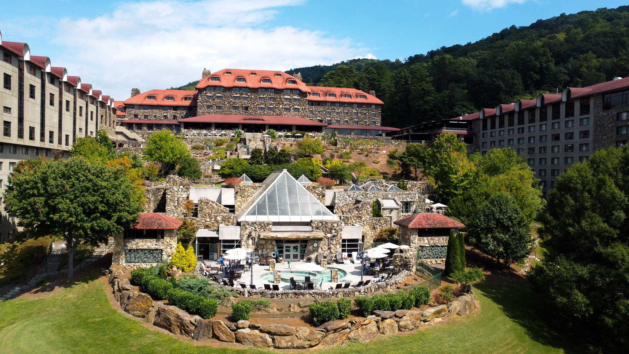 A grand mountain resort with terrace cafe features red-tiled roofs and landscaped gardens surrounding a gazebo fountain.