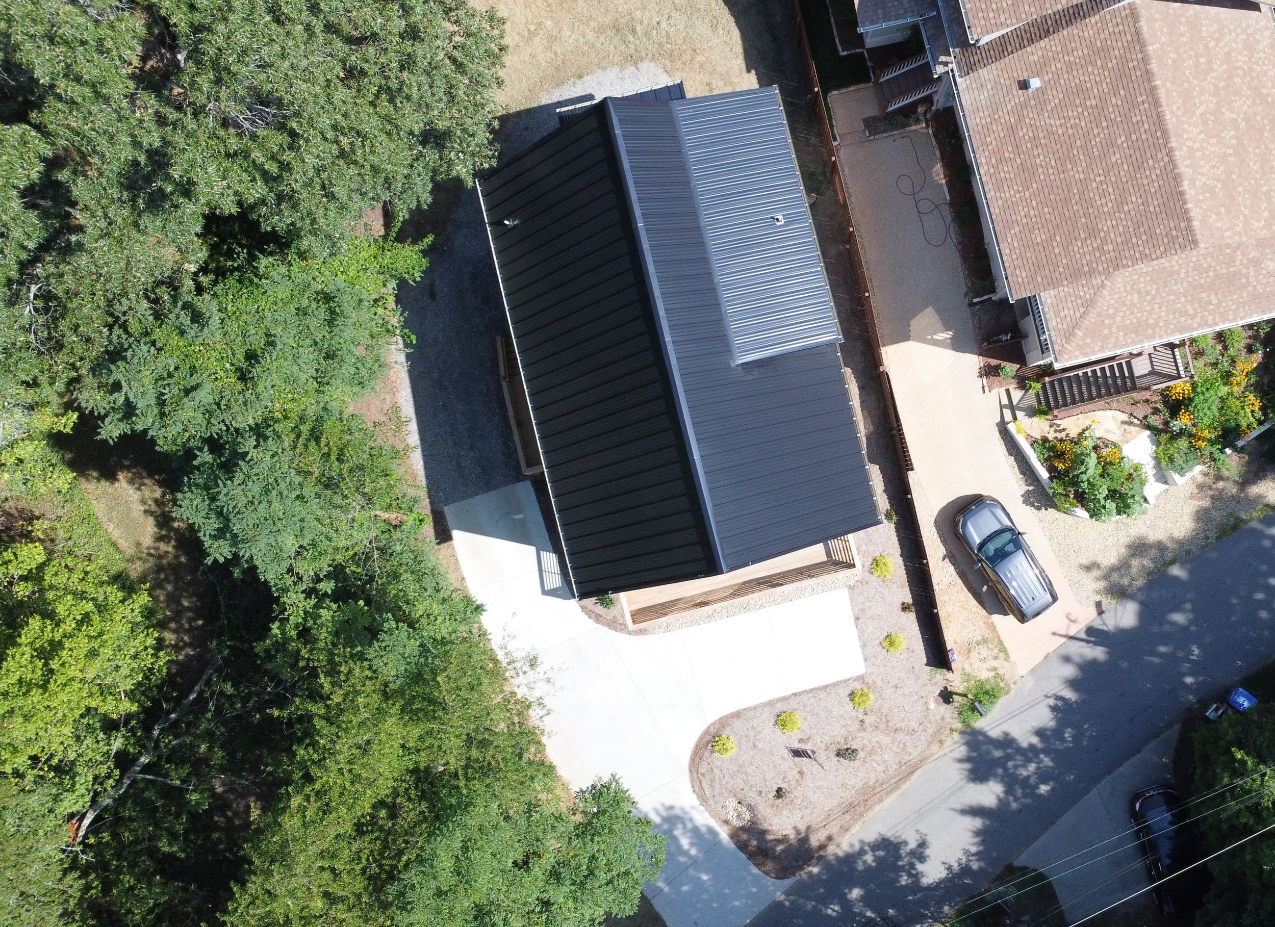 Aerial view of dark-roofed modern house with circular driveway surrounded by trees and landscaping.