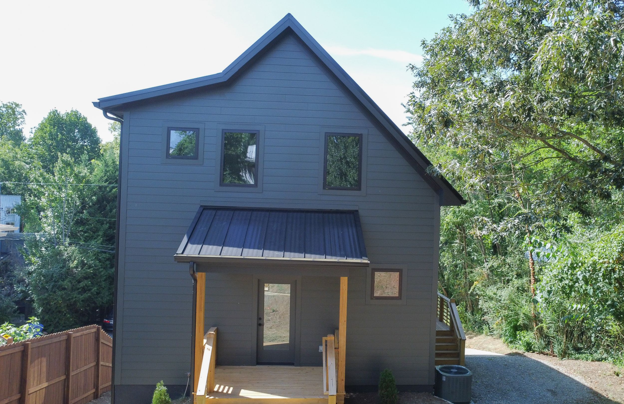 Modern gray house with blue metal roof features covered front porch and architectural details in wooded setting.