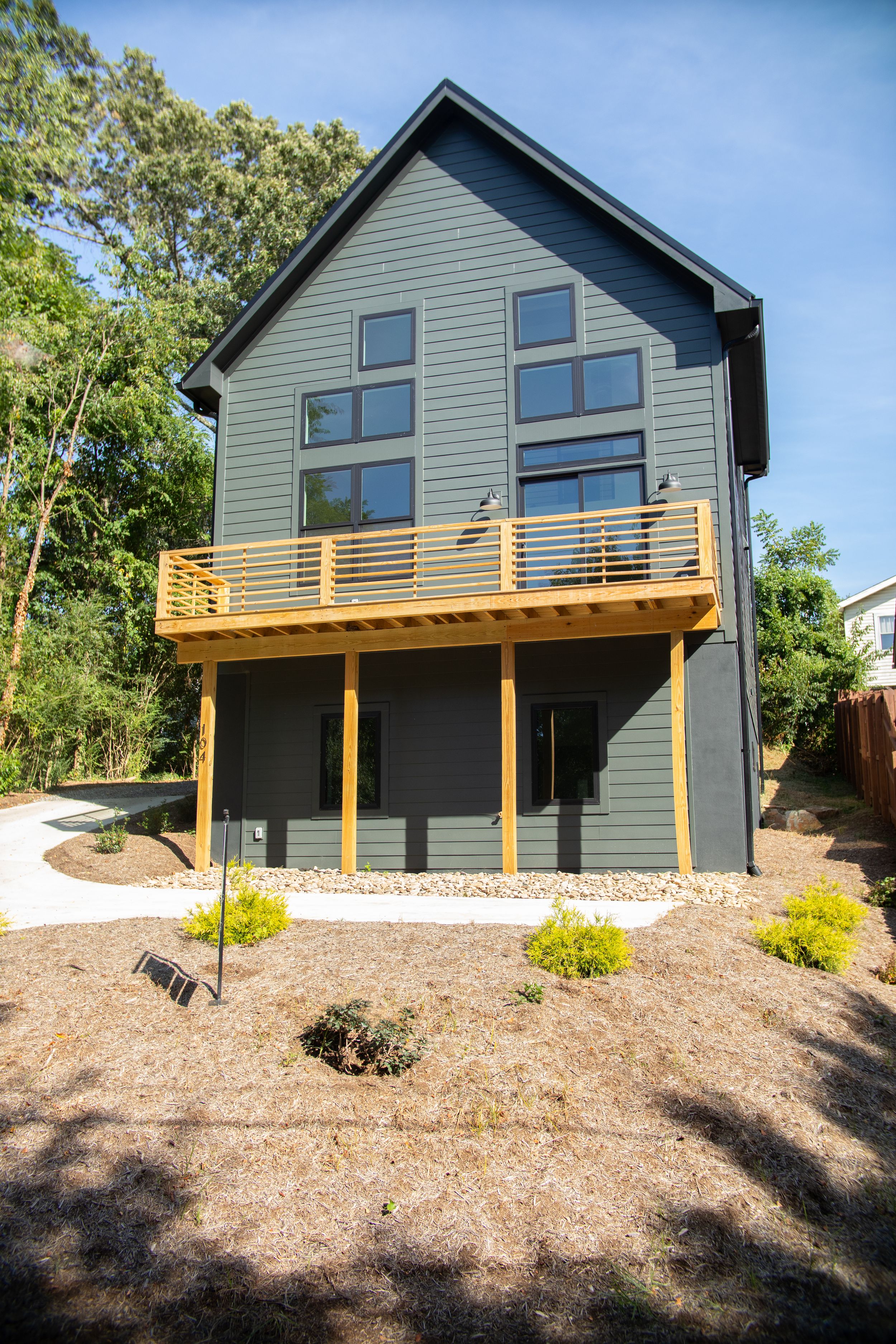 Modern two-story home with sage green siding features large windows and wooden deck above a two-car garage.