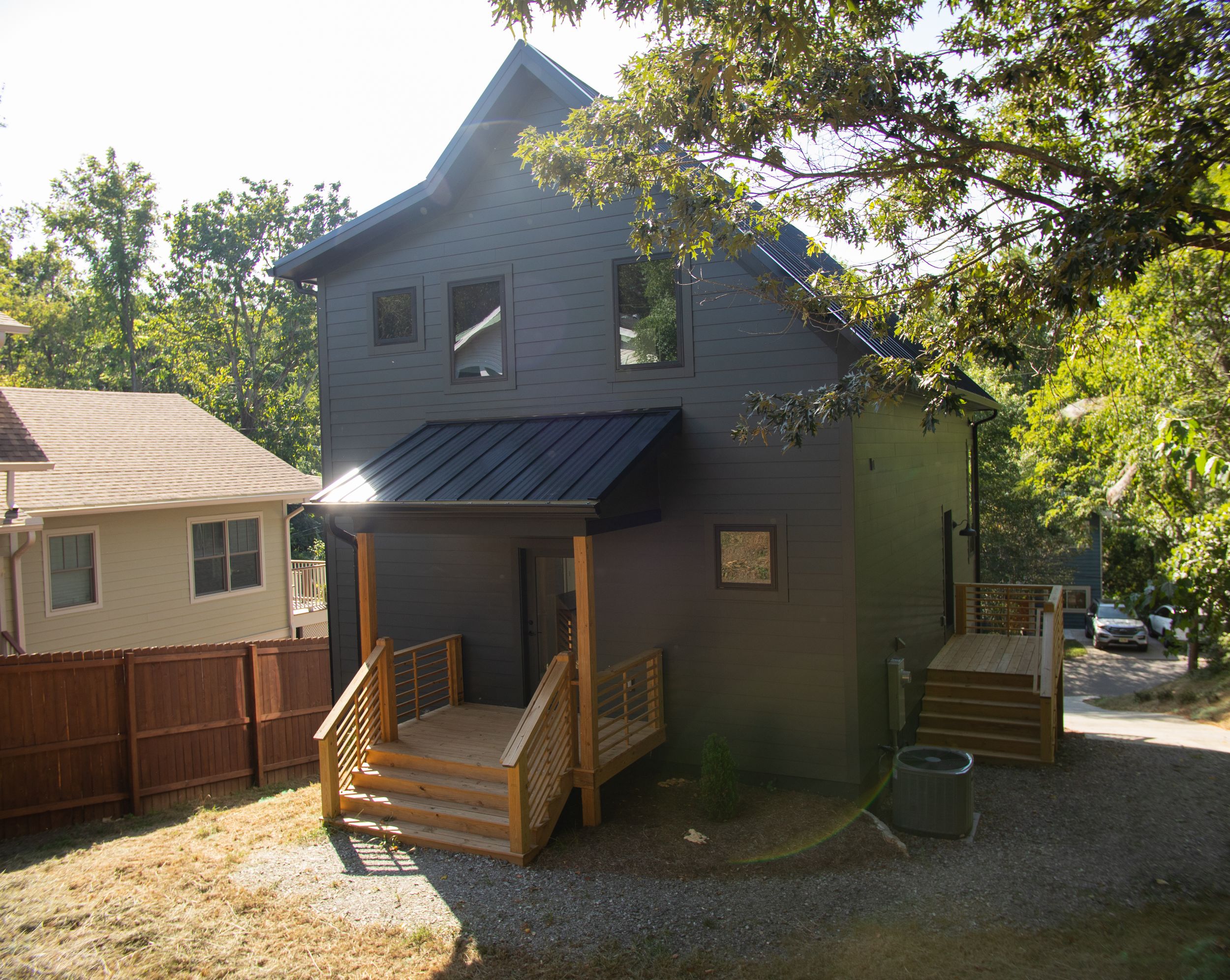 Contemporary charcoal-colored home with metal roof and wooden front porch nestled among trees in residential area.