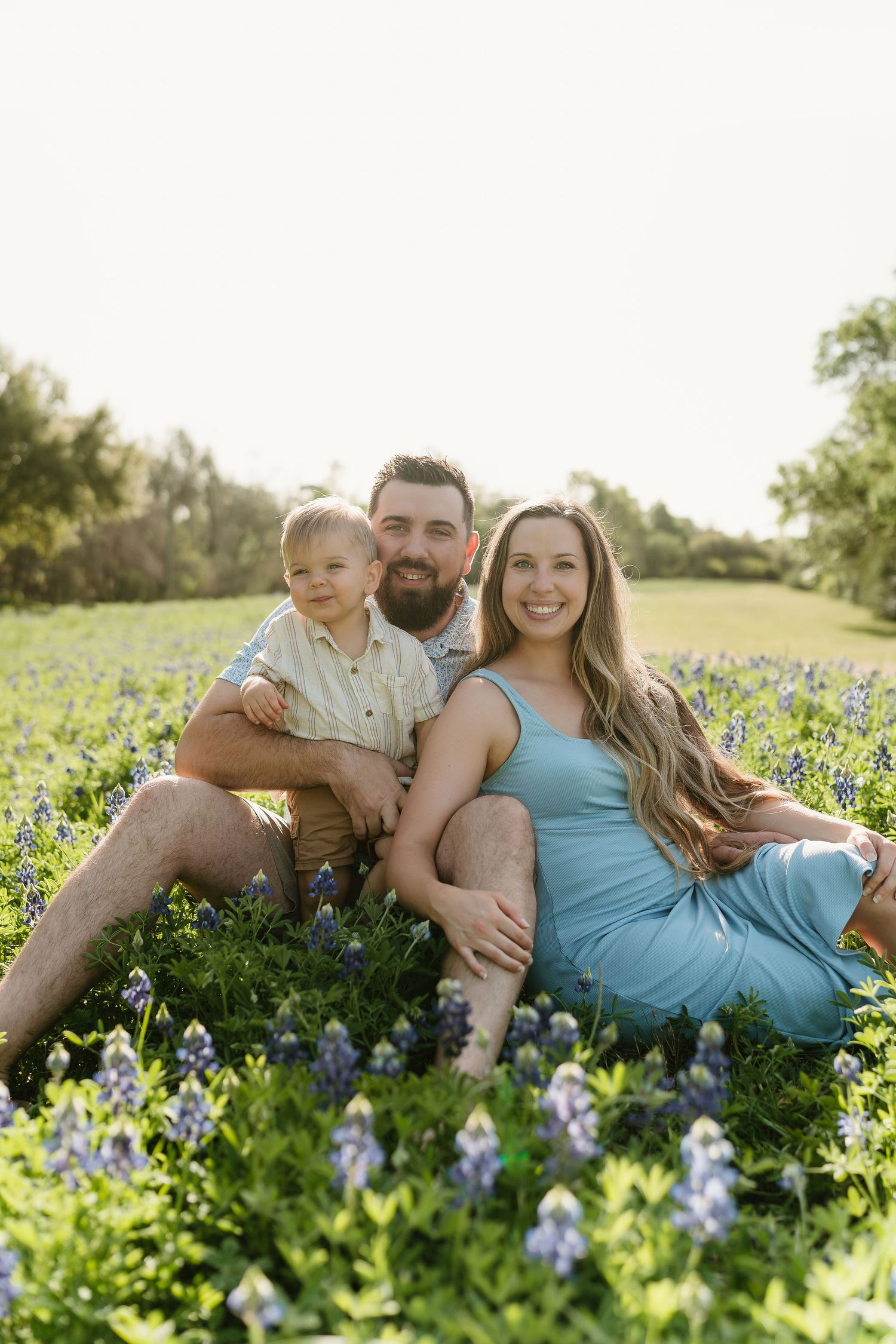 Family lounging together in a field of blooming bluebonnets during sunset.
