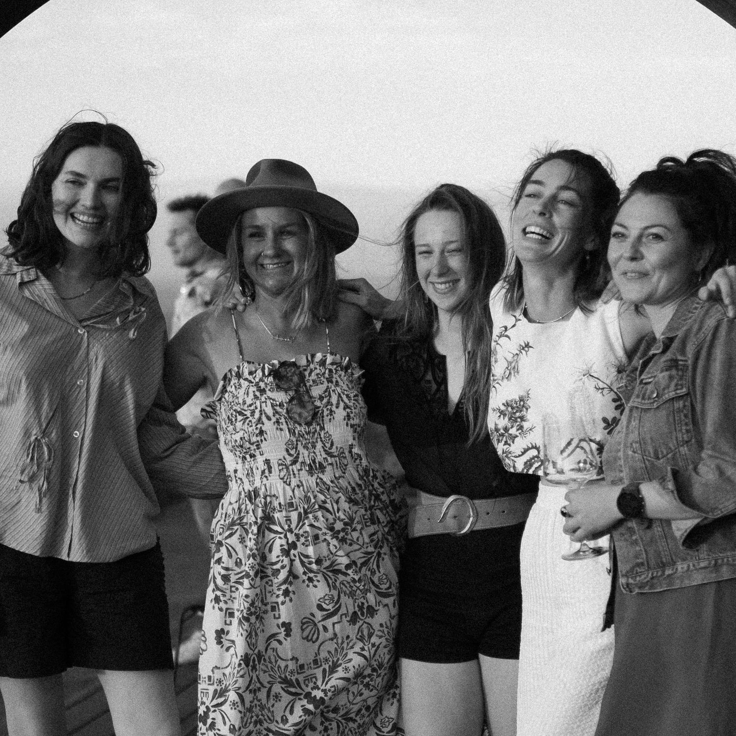Black and white photo of five happy women embracing and laughing together outdoors.
