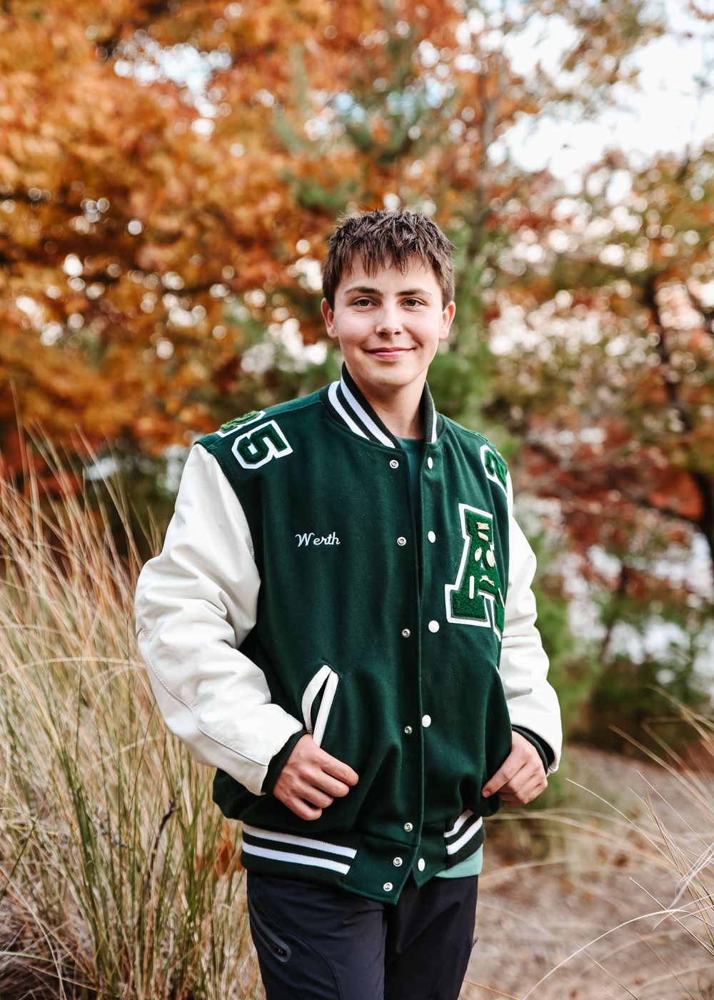 Varsity letterman jacket in green and white displayed outdoors against autumn foliage.