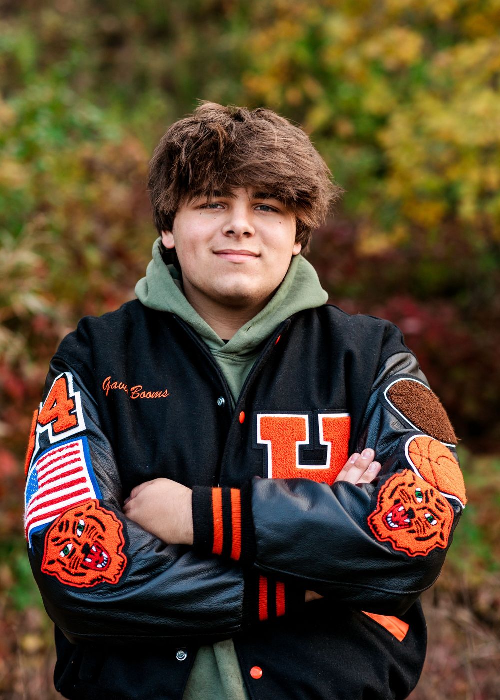 High school varsity letterman jacket with orange tiger mascots and American flag patches worn with a green hoodie underneath.